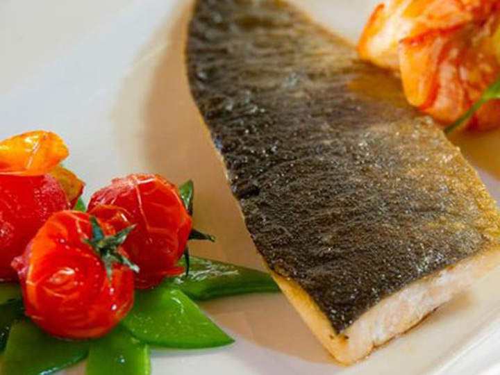 Ein Teller mit gebratenem Fischfilet, Kirschtomaten und grünen Zuckerschoten. Die Haut des Fisches ist knusprig und die Tomaten sind leicht geröstet, was der eleganten Präsentation Farbe verleiht.