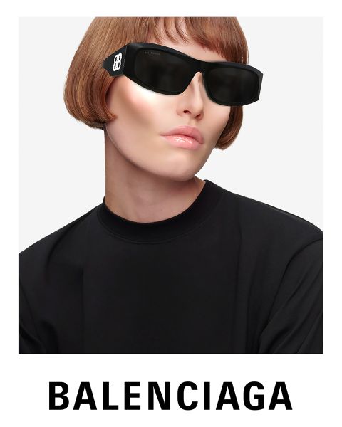 Une personne portant des lunettes de soleil noires futuristes et un haut noir pose devant un fond clair. Elle a un carré court et blond clair. Le logo Balenciaga est clairement visible en bas.