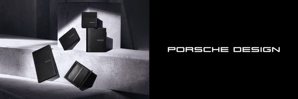Une collection d'accessoires en cuir noir de Porsche Design, comprenant des portefeuilles et des porte-cartes, est élégamment présentée sur des surfaces en béton, projetant des ombres douces. Le logo Porsche Design est bien visible sur le côté droit.