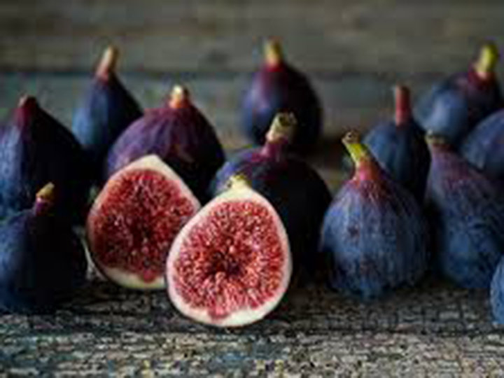 Eine Gruppe dunkelvioletter Feigen wird auf einer Holzoberfläche präsentiert. Einige Feigen sind ganz und zwei sind aufgeschnitten, sodass ihr strukturiertes, rotes Inneres mit weißen Kernen sichtbar ist. Der rustikale, erdige Hintergrund verstärkt das natürliche Aussehen des Fruchtarrangements.