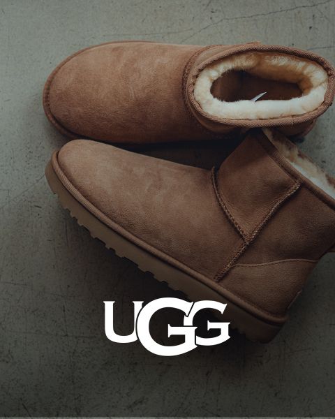 Une paire de bottes UGG en daim marron avec une doublure intérieure moelleuse, posée sur une surface grise. Le logo UGG est bien visible en bas de l'image.