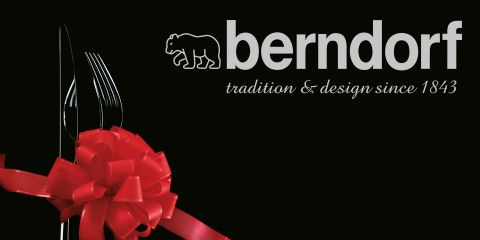 Un ensemble de couverts, composé d'une fourchette, d'un couteau et d'une cuillère, est noué avec un ruban rouge. Le texte indique « berndorf tradition & design since 1843 », avec un logo d'ours stylisé au-dessus de « berndorf ». Le fond est noir.