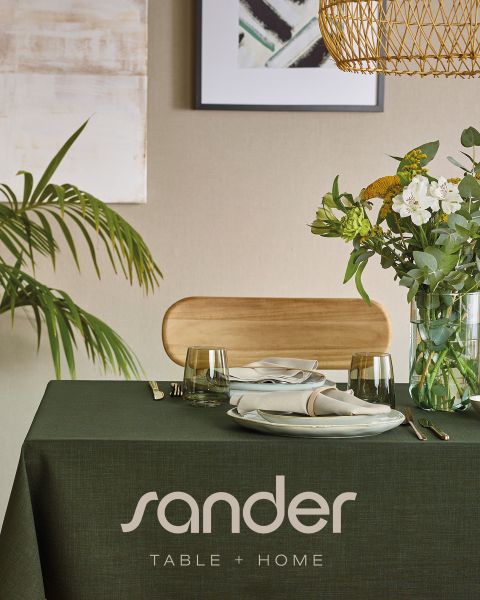 Une table à manger moderne avec une nappe verte, des assiettes, des verres, des serviettes, un arrangement floral et l'inscription « sander TABLE + HOME ».
