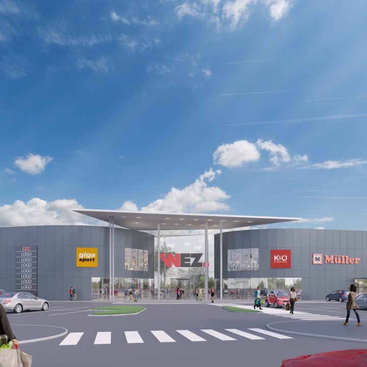 Un centre commercial moderne avec plusieurs logos de marques au-dessus des devantures de magasins, notamment Spar, Giga Sport et Müller. L'entrée est dotée d'un grand auvent et des voitures sont garées dans les rues environnantes, où l'on voit aussi des piétons. Ciel bleu éclatant avec quelques nuages.