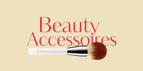 Un pinceau de maquillage avec un manche blanc et des poils bruns est placé au-dessus des mots « Accessoires de beauté » en rouge sur un fond beige.