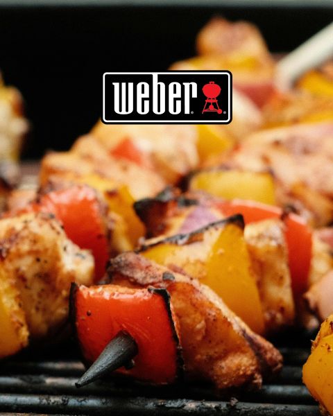 Gros plan sur des brochettes de poulet et de légumes grillées sur un barbecue. Les brochettes sont composées de morceaux de poulet avec des poivrons rouges et jaunes, ainsi que des oignons rouges. Le logo Weber est bien visible en haut au centre de l'image.