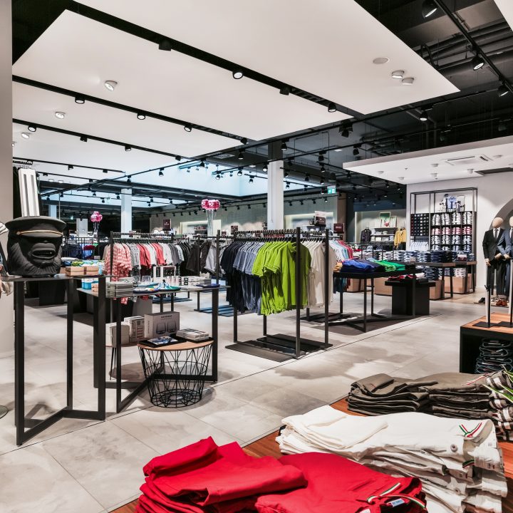 Intérieur moderne d'un magasin de vêtements avec des mannequins portant des tenues décontractées. Divers étagères présentent des chemises, des pantalons et des accessoires colorés. L'espace est bien éclairé et propose un mélange de mode décontractée et haut de gamme.