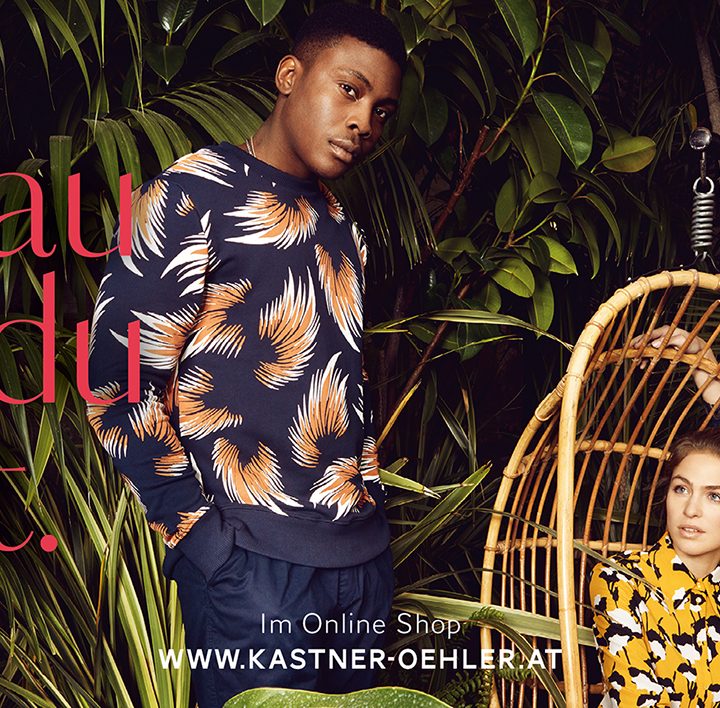 Trois mannequins en tenues stylées et à motifs se tiennent debout et sont assis au milieu d'une végétation luxuriante. Le texte est « Exactement ce que tu aimes ». En haut à droite se trouve un logo rouge avec « Kastner & Öhler ». En bas, au centre, se trouve l'URL du site web.