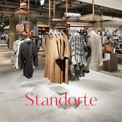 Un intérieur chic d'un magasin de vêtements avec des vêtements suspendus dans des tons neutres comme le beige et le gris. Le magasin propose une variété d'articles de mode et d'accessoires. Le mot « Emplacements » est clairement visible sur le sol.