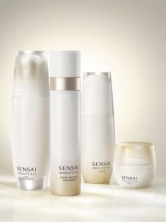 Quatre produits de soin Sensai Absolute Silk blancs et élégants, dont des flacons et un pot, sont disposés dans une lumière douce et lumineuse.