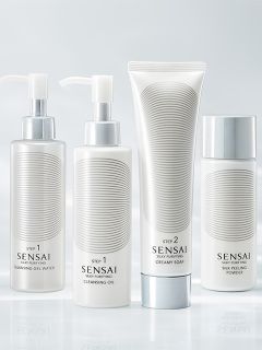 Quatre simples flacons blancs de produits de soin Sensai avec des accents argentés, étiquetés Step 1 et Step 2, disposés devant un fond doux et clair.