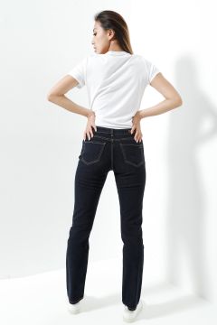 Une personne se tient devant un fond blanc et regarde au loin de la caméra. Elle porte un t-shirt blanc, un jean foncé et des baskets blanches, et a les mains sur les hanches.