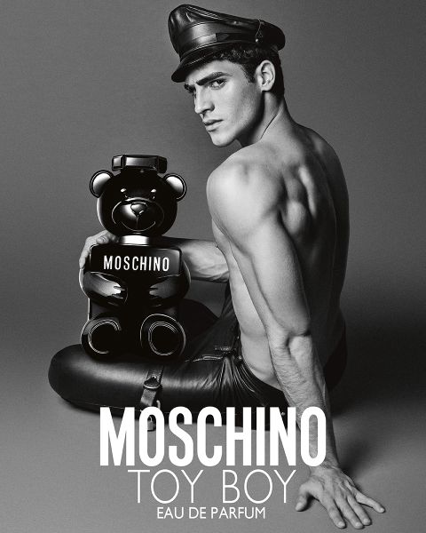 Homme torse nu en Lederhose et chapeau tenant un flacon de parfum Moschino en forme d'ours en peluche. Texte : « MOSCHINO TOY BOY EAU DE PARFUM. »