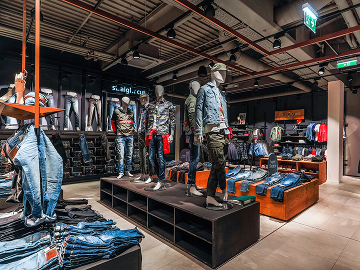 Une boutique de vêtements tendance avec des mannequins portant des tenues décontractées, notamment des jeans et des vestes. Des étagères et des présentoirs présentent une variété de vêtements en jean sous un éclairage vif, créant ainsi une atmosphère moderne et élégante.