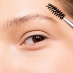 Nahaufnahme einer Person, die mit einem Brauenpinsel Augenbrauengel aufträgt, um ihre Augenbrauen zu formen. Die Haut ist glatt und die Augenbrauen sind ordentlich gepflegt. Der Fokus liegt auf dem Augen- und Brauenbereich und betont eine natürliche Schönheitsroutine.