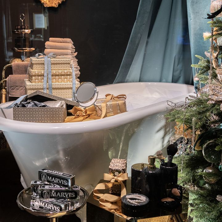 Une baignoire décorée est entourée de produits de bain et d'articles de toilette de luxe. À côté, se dresse un sapin de Noël orné. Les serviettes et les accessoires de bain sont soigneusement disposés, créant une atmosphère festive et opulente.