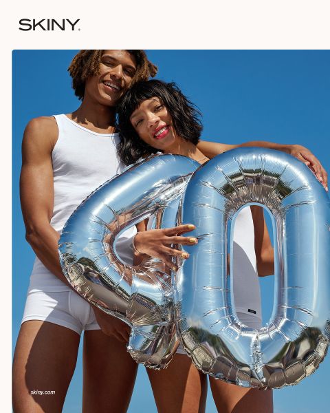 Deux personnes en sous-vêtements blancs tiennent en souriant un ballon argenté avec le chiffre "40" devant un ciel bleu éclatant.