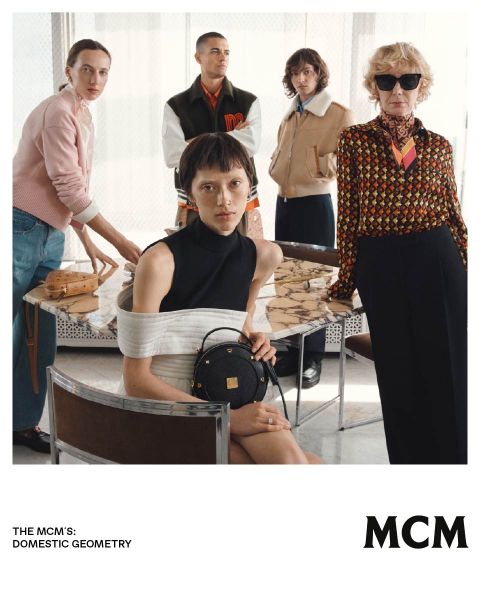 Cinq personnes élégantes posent dans un intérieur autour d'une table en marbre, présentant des sacs et de la mode MCM dans une ambiance moderne et élégante.