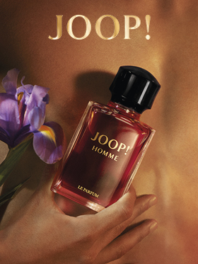 Une bouteille de JOOP! Homme Le Parfum est tenue devant un arrière-plan flou avec une fleur d'iris violette. Le logo doré de "JOOP!" est clairement visible en haut. L'image transmet élégance et luxe.