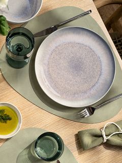 Couvert de table avec un set de table vert, une assiette en céramique, un verre, une fourchette, un couteau, un petit bol avec de l'huile et de l'aneth, ainsi qu'une serviette en tissu verte avec un rond de serviette.