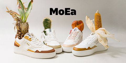 Une exposition de quatre paires de baskets MoEa, chacune ornée de différents éléments naturels tels que des feuilles d'ananas, un cactus, un épi de maïs et une pomme. Les baskets ont des bases blanches avec des accents colorés sur un fond neutre.