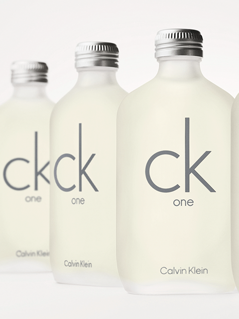 Quatre flacons mats de Calvin Klein CK One sont visibles devant un fond clair. Les flacons portent l'inscription grise « ck one » et des bouchons argentés.