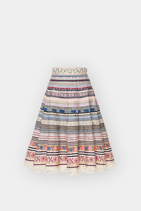 Une jupe trapèze arrivant au genou avec des rayures horizontales colorées, des motifs entrelacés et des broderies florales sur fond blanc.