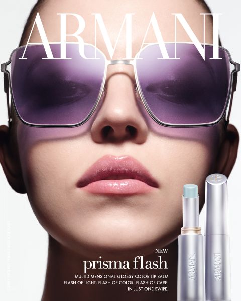 Gros plan d'une femme portant des lunettes de soleil surdimensionnées et des lèvres roses brillantes, avec deux baumes à lèvres Armani Prisma Flash visibles en bas à droite.