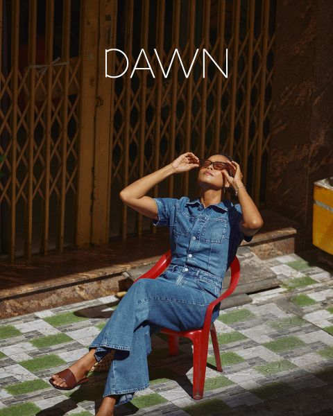 Une femme en vêtements en jean est assise sur une chaise rouge à l'extérieur, penche la tête en arrière et ajuste ses lunettes de soleil. Au-dessus de sa tête apparaît le texte "DAWN".