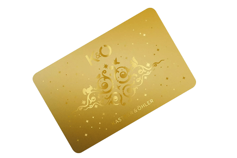 Une carte dorée ornée de volutes décoratives et d'étoiles, sur laquelle sont imprimés en lettres élégantes "K&O" et "KASTNER & ÖHLER". La carte présente un design luxueux et festif.