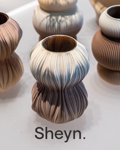 Un vase sculptural en céramique avec une texture ondulée dans des tons neutres, y compris le lettrage en gras Sheyn".