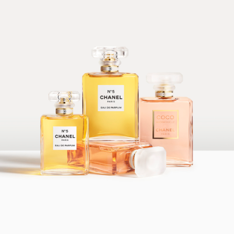 Quatre flacons de parfum Chanel, dont deux No. 5 Eau de Parfum avec un liquide doré et deux Coco Mademoiselle, sont disposés sur une surface blanche. Les parfums se trouvent dans d'élégants flacons en verre avec des bouchons carrés, projetant des ombres douces.