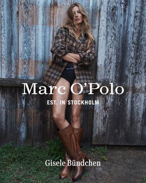 Une femme portant une chemise à carreaux, un short noir et des bottes marron se tient devant un mur en bois patiné. Le texte est le suivant : "Marc O'Polo EST. IN STOCKHOLM Gisele Bündchen.