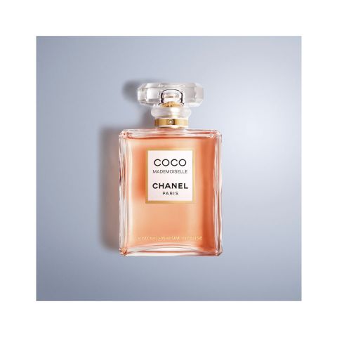 Une bouteille de Chanel Coco Mademoiselle Eau de Parfum Intense avec un corps rectangulaire clair et un bouchon à facettes. L'inscription "Coco Mademoiselle Chanel Paris" figure sur le devant. La bouteille repose sur une surface bleu-gris clair.