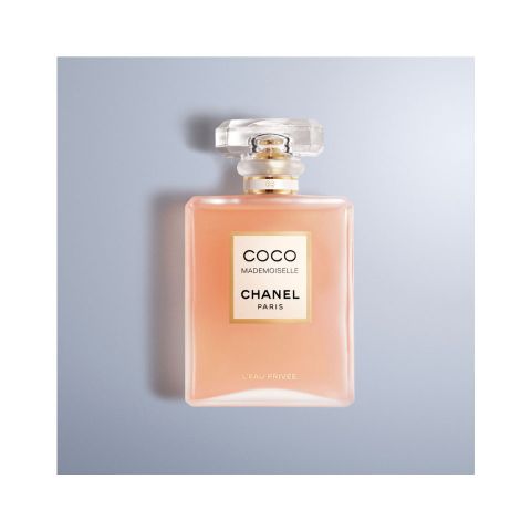 Un flacon de parfum Chanel Coco Mademoiselle L'Eau Privée sur un fond bleu clair. Le flacon est rose avec une étiquette dorée et un bouchon transparent et carré.