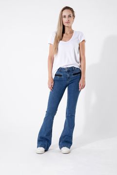 Une personne portant un t-shirt blanc et un jean pattes d'éléphant bleu se tient devant un fond blanc uni. Elle a les cheveux longs et porte des baskets blanches. Elle pose avec une main dans la poche et l'autre sur la hanche.