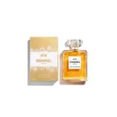 Une bouteille de Chanel N°5 Eau de Parfum est présentée à côté de son emballage doré et blanc. Le flacon est rectangulaire, possède un bouchon transparent et contient un parfum ambré. L'emballage est élégant et emblématique.