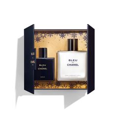Boîte ouverte contenant deux flacons de Bleu de Chanel : un flacon de parfum à gauche et un flacon de soin hydratant pour la peau à droite. L'arrière-plan présente un motif doré artistique. La boîte est sombre avec des détails dorés.