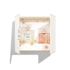 Dans une boîte cadeau blanche ouverte, on peut voir deux flacons de parfum portant l'inscription "Coco Mademoiselle Chanel Paris". Le flacon de gauche est rempli d'un liquide clair, celui de droite d'un liquide rose. L'arrière-plan est orné d'un motif de flocons de neige dorés.