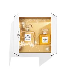Boîte blanche ouverte avec deux flacons du parfum Chanel N°5 sur un fond doré avec des motifs de flocons de neige. Le plus grand flacon porte l'inscription « Eau de Parfum », le plus petit porte l'inscription « L'Eau ».
