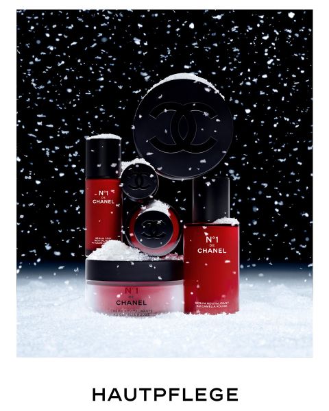 Sur la neige, devant un fond sombre, on aperçoit des produits de soin de la peau Chanel avec un emballage rouge et noir. Des flocons de neige tombent autour d'eux. En bas, on peut lire le mot « SOIN DE LA PEAU ».