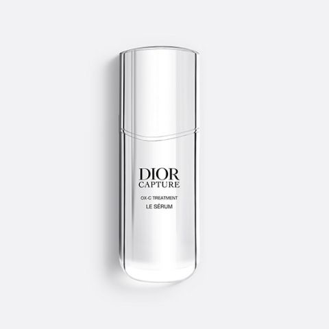 Un flacon Dior Capture OX-C Treatment Le Sérum, fin et translucide. Le flacon est haut et incurvé, avec un design minimaliste et un texte noir sur le devant. Sur un fond gris clair.