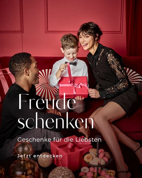Une famille composée d'un homme, d'une femme et d'un enfant est assise dans une pièce rouge. L'enfant ouvre avec excitation une boîte cadeau rouge. Le texte sur l'image est : « Offrir de la joie, des cadeaux pour les proches, À découvrir maintenant. ».