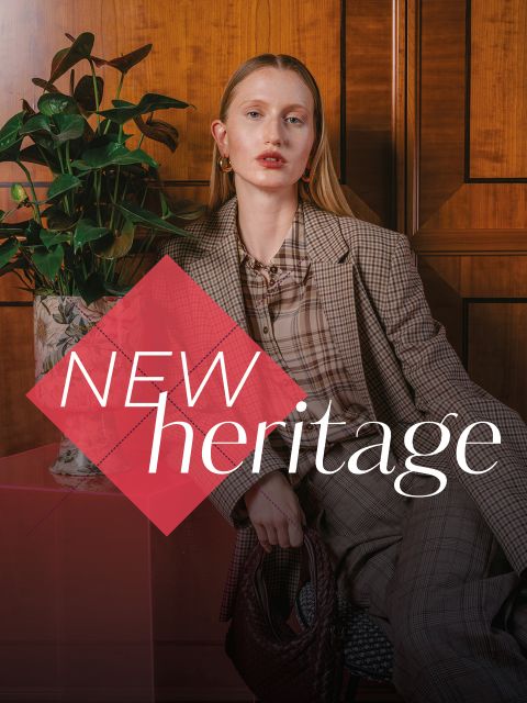 Une femme en costume à carreaux est assise à côté d'une plante, avec le texte "NEW heritage" superposé devant elle.