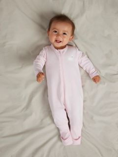 Un bébé est allongé sur une couverture blanche et porte un pull en tricot rose clair avec un col Claudine et un pantalon assorti, ainsi que des chaussettes couleur crème.