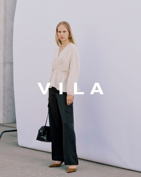 Cinq femmes en tenues décontractées, notamment des jeans et des hauts de couleurs neutres, se tiennent proches les unes des autres et sourient devant un fond uni. Le texte superposé est "Vila Clothes".