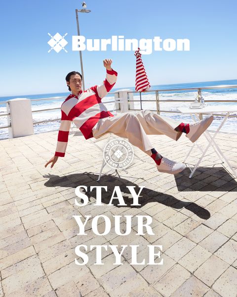 Un homme et une femme en tenues élégantes posent avec assurance sur un banc blanc devant un mur vert avec les textes "Burlington" et "Affirmez votre style" au-dessus et en dessous d'eux.