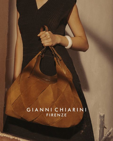 Personne portant un long trench-coat noir en cuir et des lunettes de soleil, tenant un petit sac à motif léopard. Le fond est gris, avec le texte "GIANNI CHIARINI FIRENZE" en blanc au-dessus de l'image.