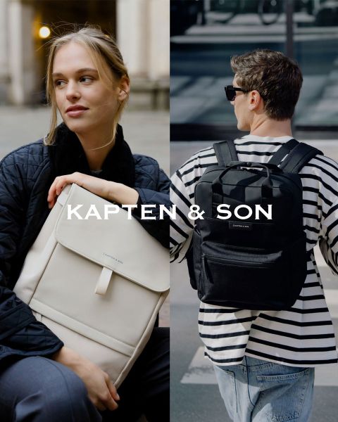 Une femme et un homme se sourient à l'extérieur. La femme porte un bonnet vert et un manteau beige et tient un sac noir à la main. L'homme porte une veste marron et un sac couleur crème. Au milieu, il y a écrit « Kapten & Son ».