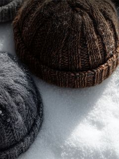 Deux bonnets tricotés, un marron et un gris foncé, sont posés sur de la neige blanche en plein soleil.